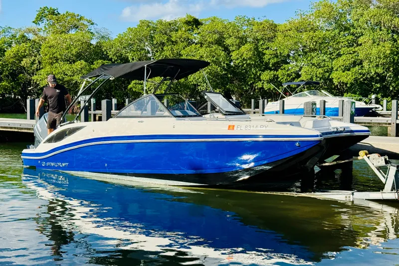 Slide: The Image of 2015 Starcraft Crossover 250 SCX OB boat docked, featuring blue and white design with canopy. - 11
