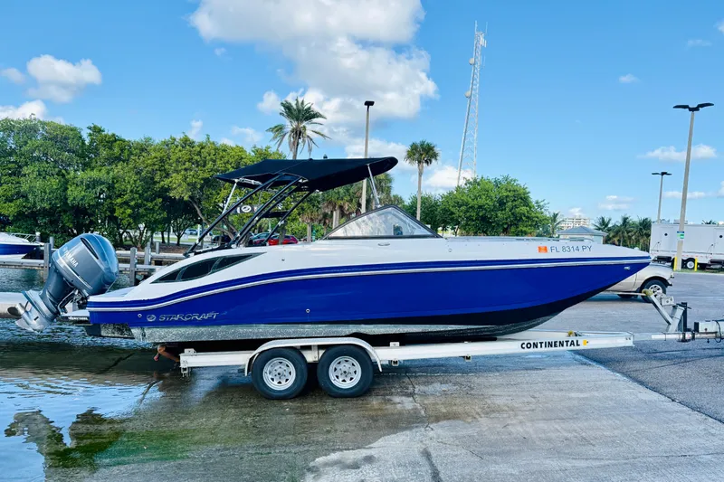 Slide: The Image of 2015 Starcraft Crossover 250 SCX OB boat on trailer, blue and white design, parked outdoors. - 2