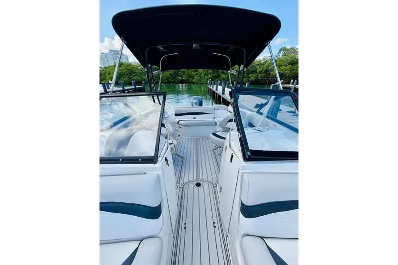 Slide: The Image of 2015 Starcraft Crossover 250 SCX OB boat interior with seating and canopy, docked by lush greenery. - 26