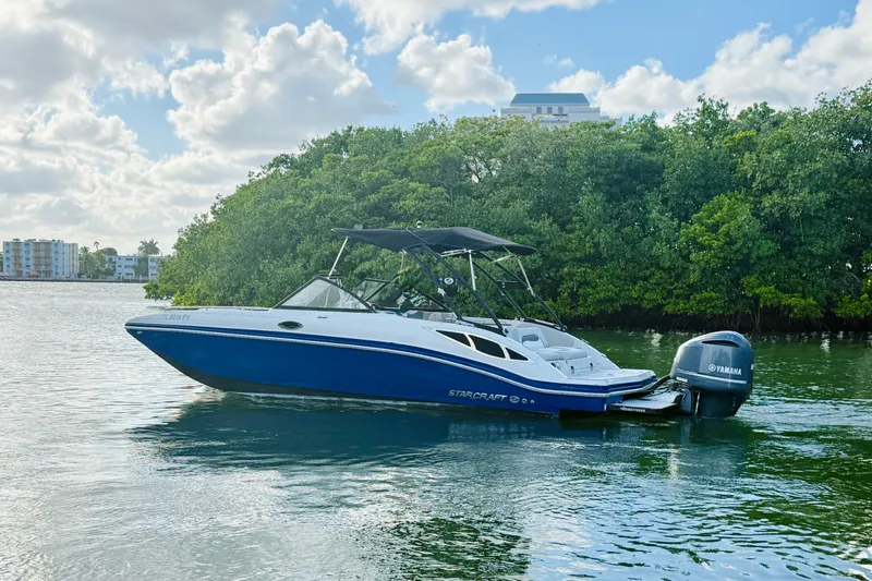 Slide: The Image of 2015 Starcraft Crossover 250 SCX OB boat on calm water, surrounded by lush greenery. - 38