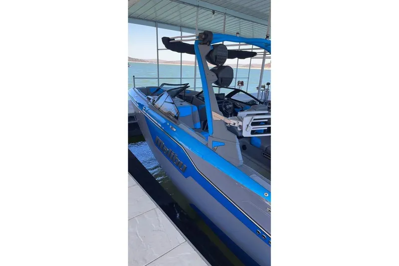Slide: The Image of 2022 Malibu M220 boat in blue, docked by a serene lake. - 3