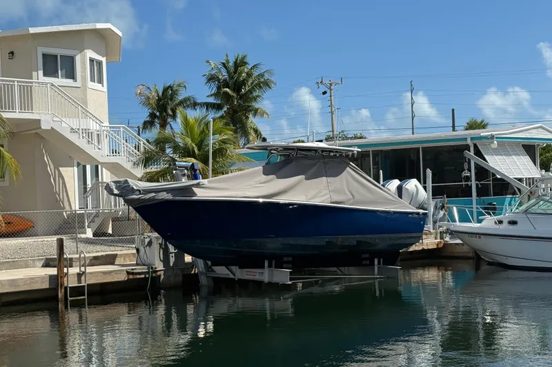 Slide: The Image of 2024 Valhalla Boatworks V-29 Hybrid covered, docked near waterfront homes and palm trees. - 2