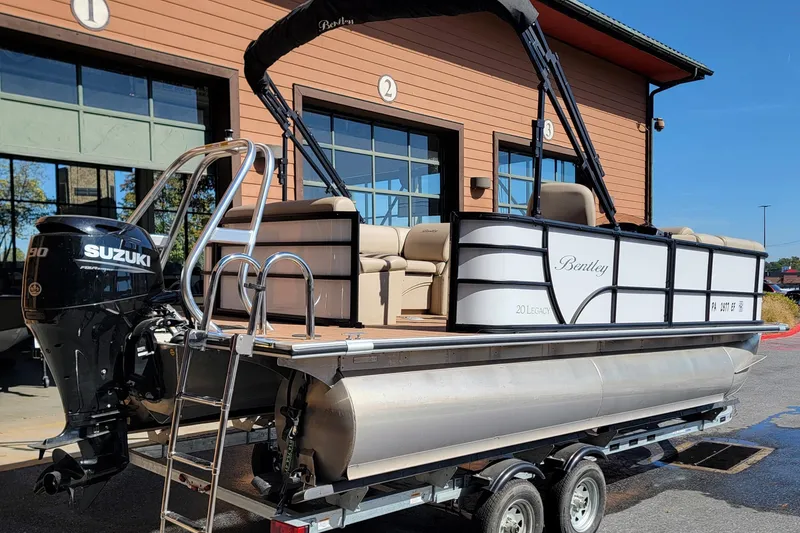 Slide: The Image of 2024 Bentley Pontoons Legacy Cruise with Suzuki engine on trailer, parked outside a building. - 2