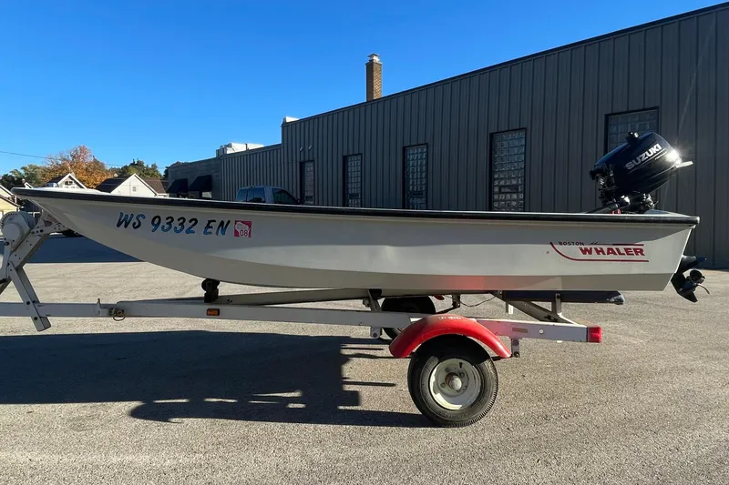 Slide: The Image of 1993 Boston Whaler Sport 11 boat on trailer, parked outdoors with Suzuki outboard motor. - 2