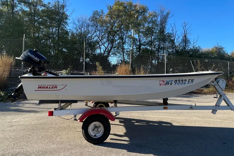 Slide: The Image of 1993 Boston Whaler Sport 11 boat on trailer, with Suzuki outboard motor, parked outdoors. - 3