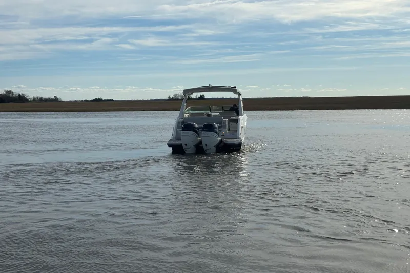 Slide: The Image of 2023 Sea Ray 310 SLX boat cruising on a calm lake under a clear sky. - 30