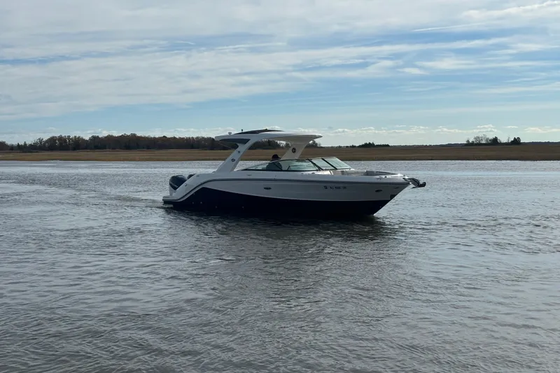 Slide: The Image of 2023 Sea Ray 310 SLX boat cruising on a calm lake under a partly cloudy sky. - 31