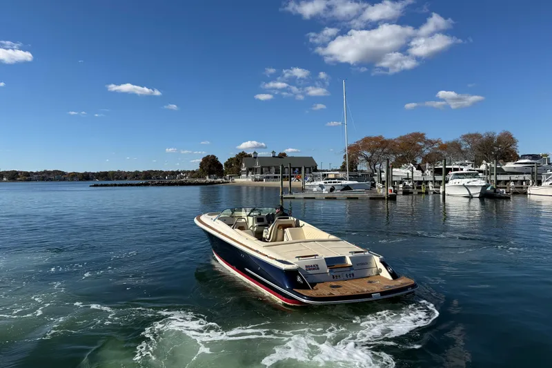 Slide: The Image of 2018 Chris-Craft Launch 30 boat on calm water near a marina under a clear blue sky. - 4