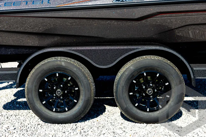 Slide: The Image of 2026 Skeeter ZXE20 trailer with dual black alloy wheels on gravel surface. - 14