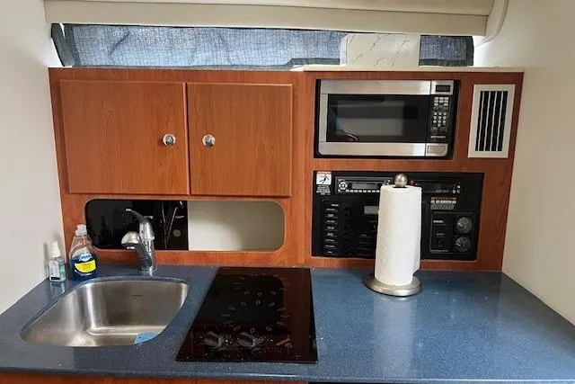 Slide: The Image of 2006 Bayliner 325 boat kitchen with sink, stove, microwave, and storage cabinets. - 13