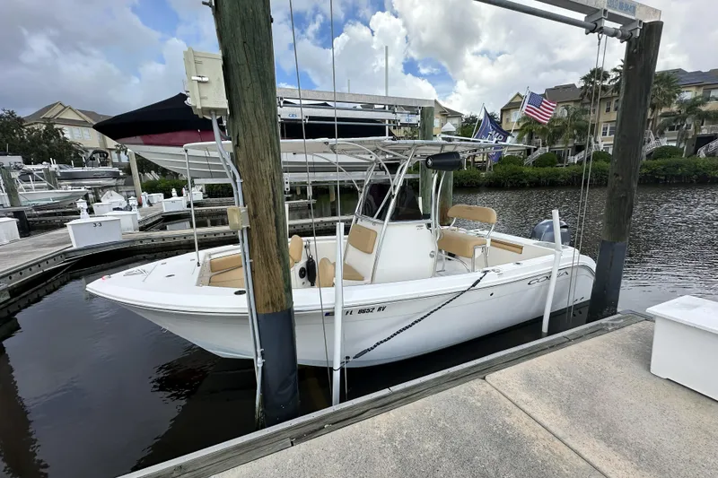 Slide: The Image of 2019 Cobia 220 Center Console boat docked at marina with flags and buildings in background. - 2