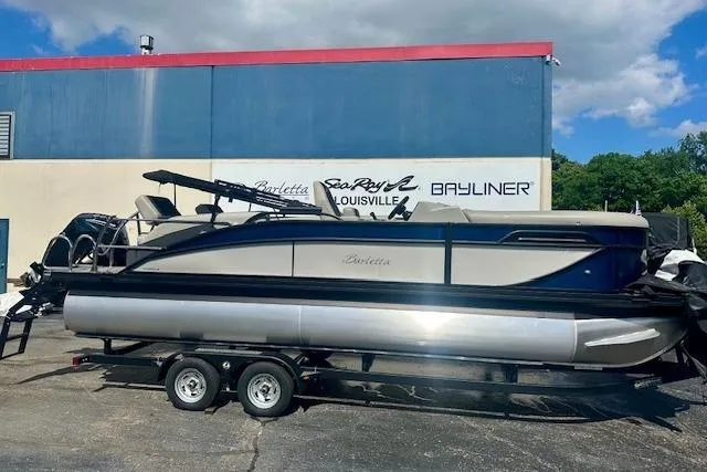 The Image of 2026 Barletta C22M pontoon boat on trailer, parked outside dealership under blue sky. - 0