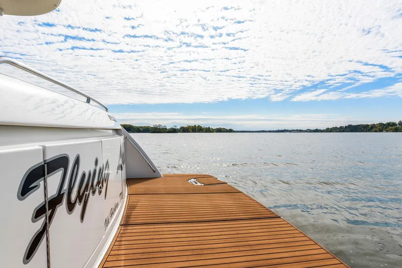 Slide: The Image of 2004 Carver 570 Voyager Pilothouse yacht on serene lake with wooden deck and cloudy sky. - 59