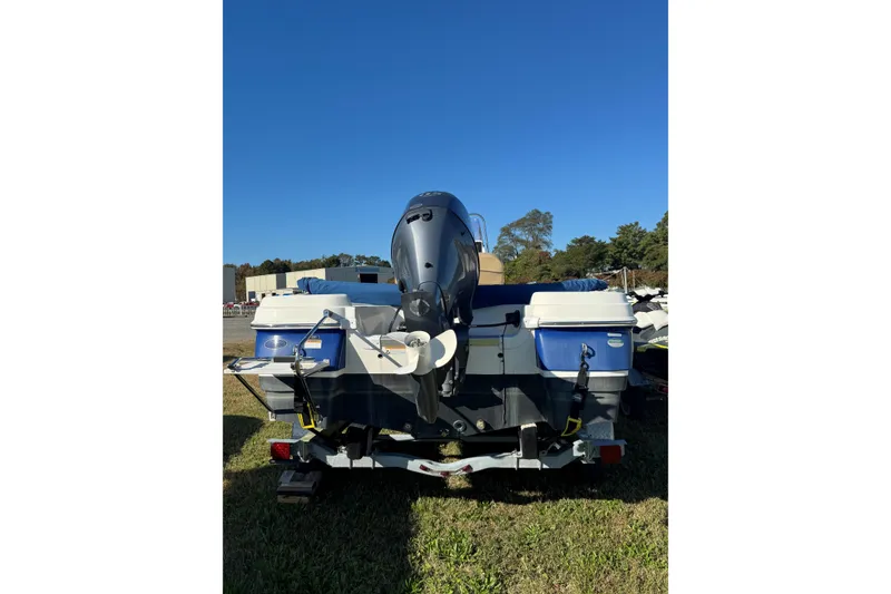 Slide: The Image of 2019 NauticStar 211 Hybrid boat with outboard motor, parked on grass under clear blue sky. - 2