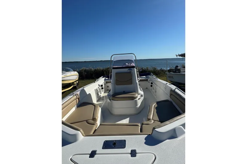 Slide: The Image of 2019 NauticStar 211 Hybrid boat with seating, docked by a serene lake under clear blue skies. - 4