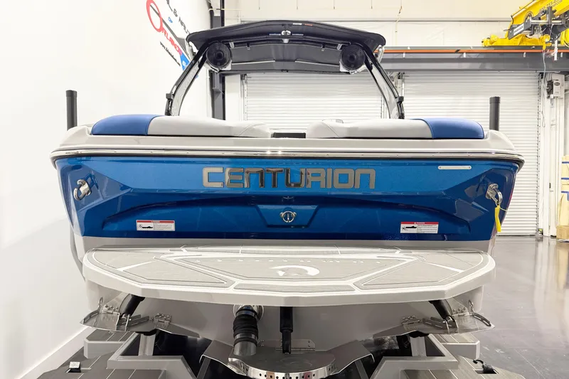 The Image of 2025 Centurion Nv233 boat, blue exterior, rear view in a showroom setting. - 1