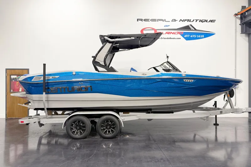 Slide: The Image of 2025 Centurion Nv233 boat in showroom, blue and white design on trailer. - 3