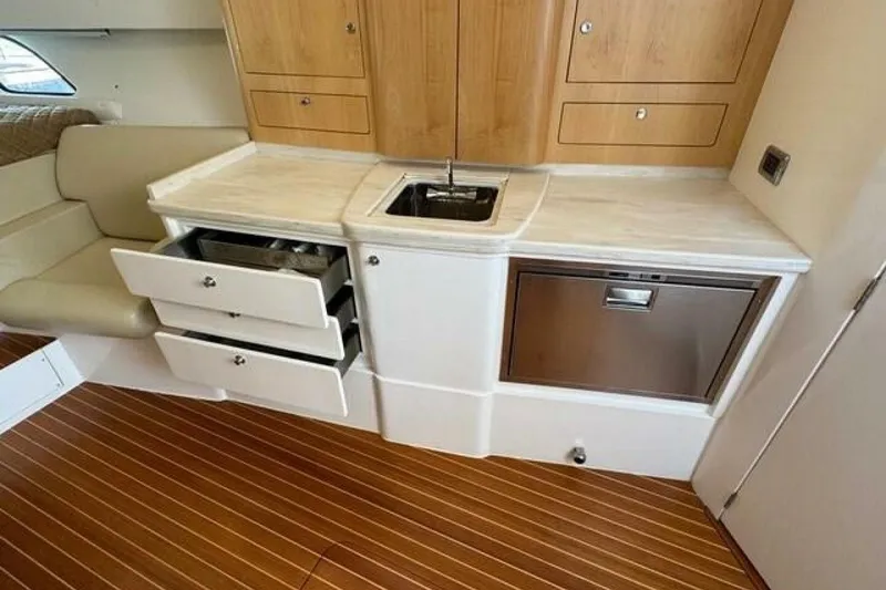 Slide: The Image of 2019 Intrepid 430 Sport Yacht interior with kitchenette, featuring sink, drawers, and wood cabinetry. - 12