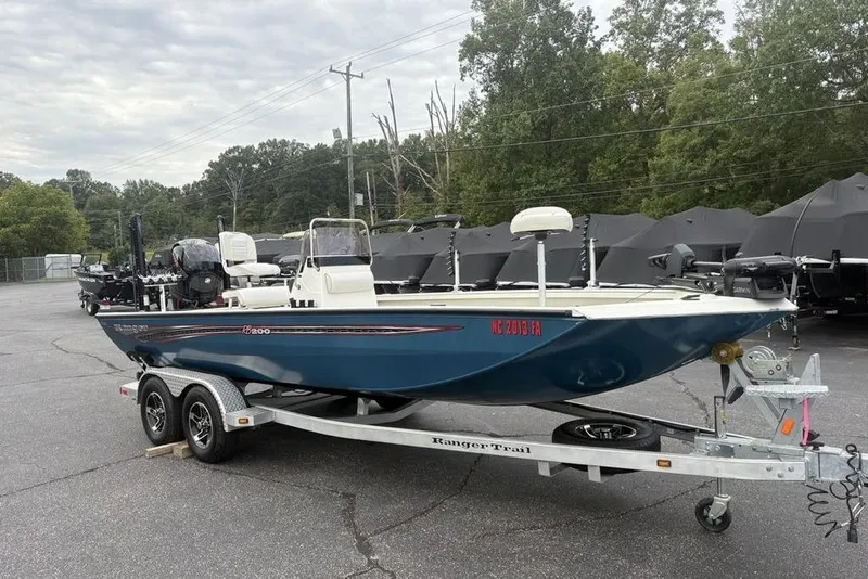 Slide: The Image of 2022 Ranger RB200 boat on trailer in parking lot, surrounded by trees and other boats. - 1