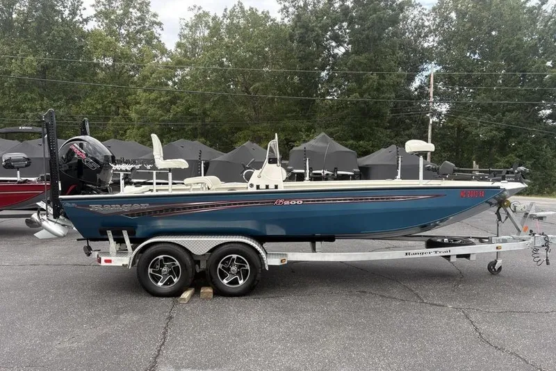 Slide: The Image of 2022 Ranger RB200 boat on trailer, parked outdoors with trees in background. - 2