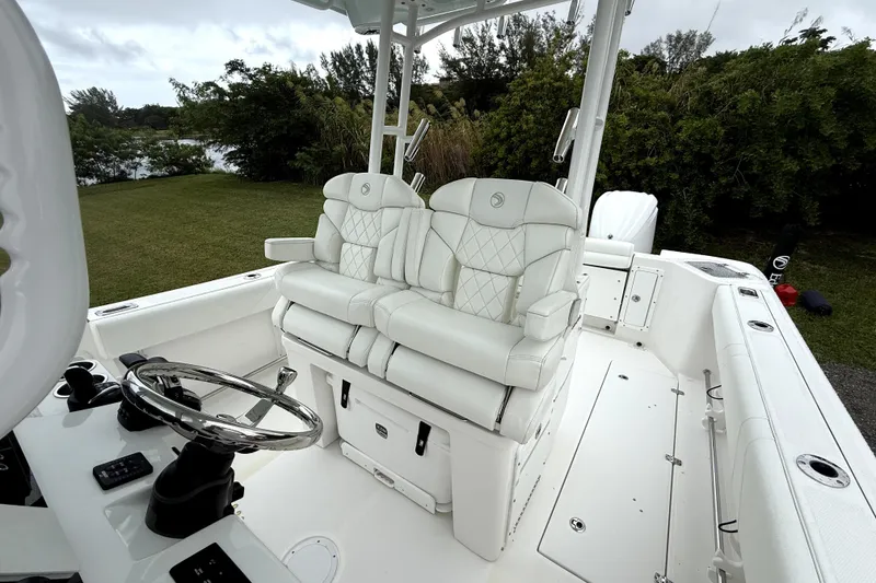 Slide: The Image of 2023 Edgewater 285CC boat interior with white seating and steering wheel, surrounded by greenery. - 12