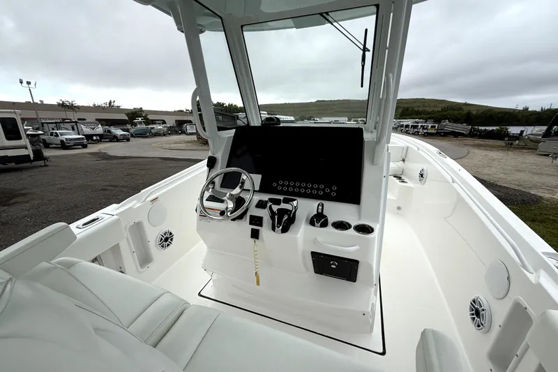 Slide: The Image of 2023 Edgewater 285CC boat interior with modern helm and seating, parked outdoors. - 17