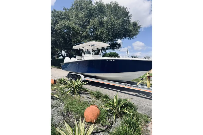 Slide: The Image of 2005 Jupiter 31 boat on trailer, parked near lush greenery and trees. - 14