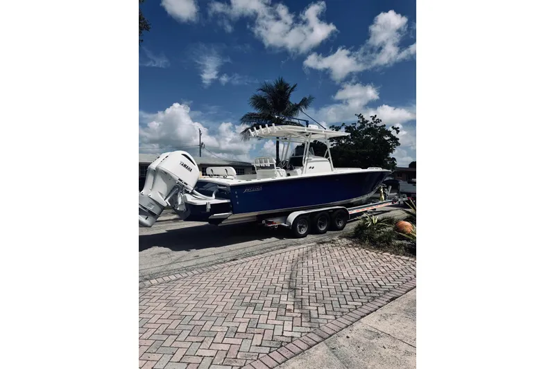Slide: The Image of 2005 Jupiter 31 boat on trailer, blue hull, dual Yamaha engines, parked on brick driveway. - 15