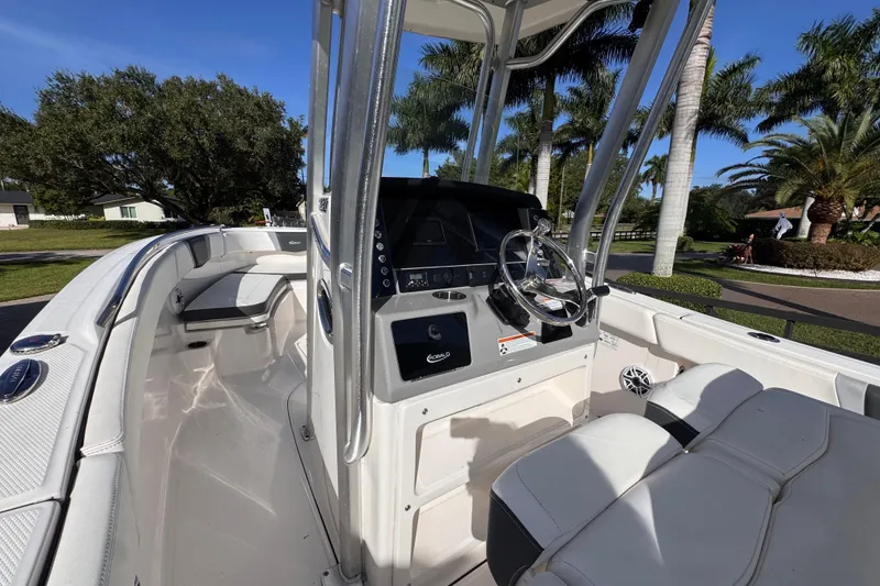 Slide: The Image of 2022 Robalo R230 Center Console boat interior with steering wheel and seating, surrounded by palm trees. - 48