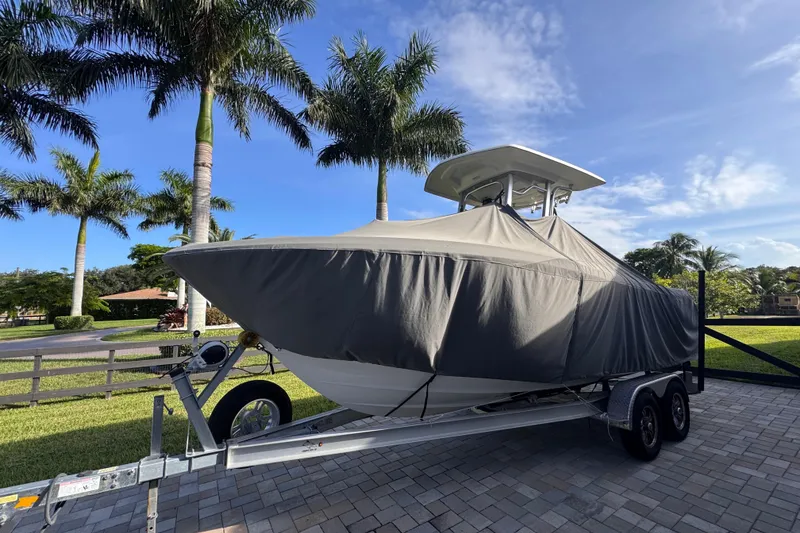 Slide: The Image of 2022 Robalo R230 Center Console boat covered on trailer, surrounded by palm trees. - 62