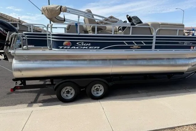 Slide: The Image of 2023 Sun Tracker Fishin' Barge 20 DLX pontoon boat on trailer, parked outdoors. - 2