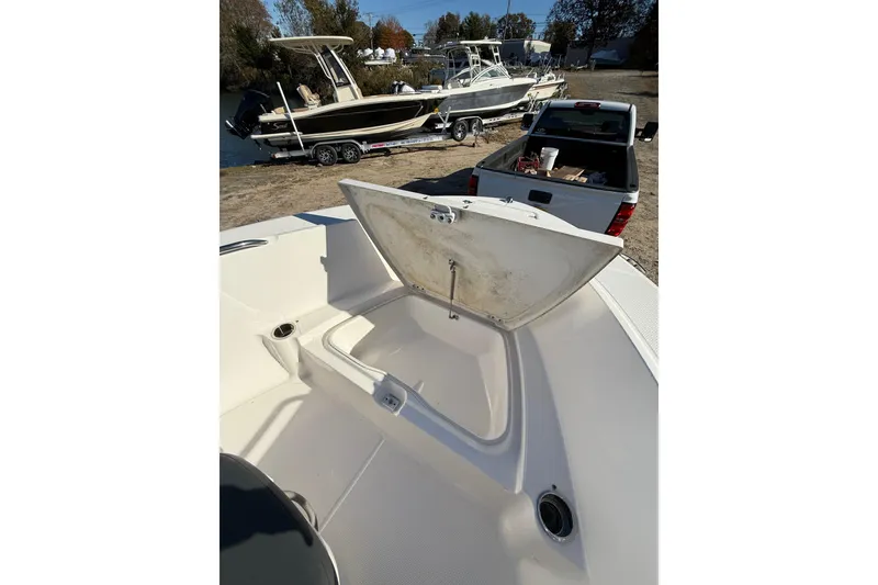 Slide: The Image of 2022 Robalo R180 Center Console boat with open storage compartment, parked near a truck. - 7
