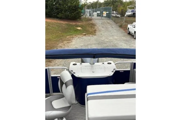 Slide: The Image of 2022 Bennington 22SXSAPG pontoon boat interior with seating and console, parked on gravel. - 5