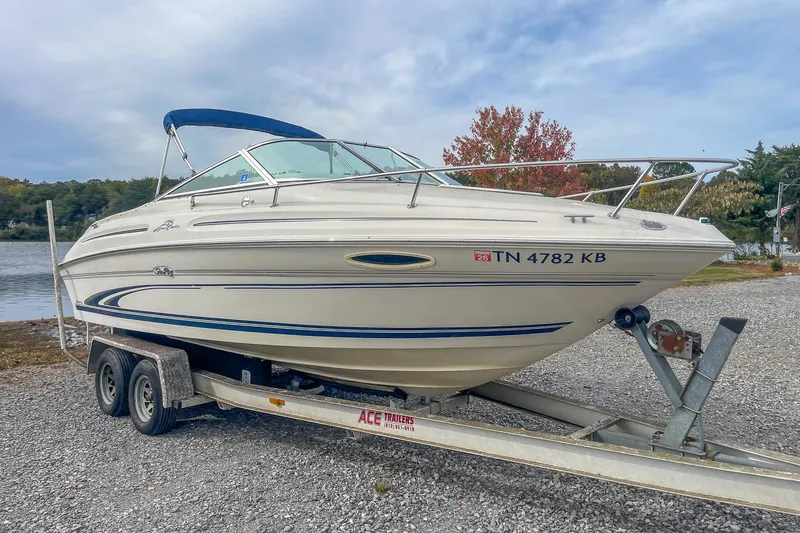 The Image of 1999 Sea Ray 215 Express Cruiser on trailer by a lake, ready for boating. - 1