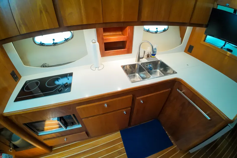 Slide: The Image of 1999 Tiara Yachts 3500 Express galley with stove, sink, and wooden cabinetry. - 100