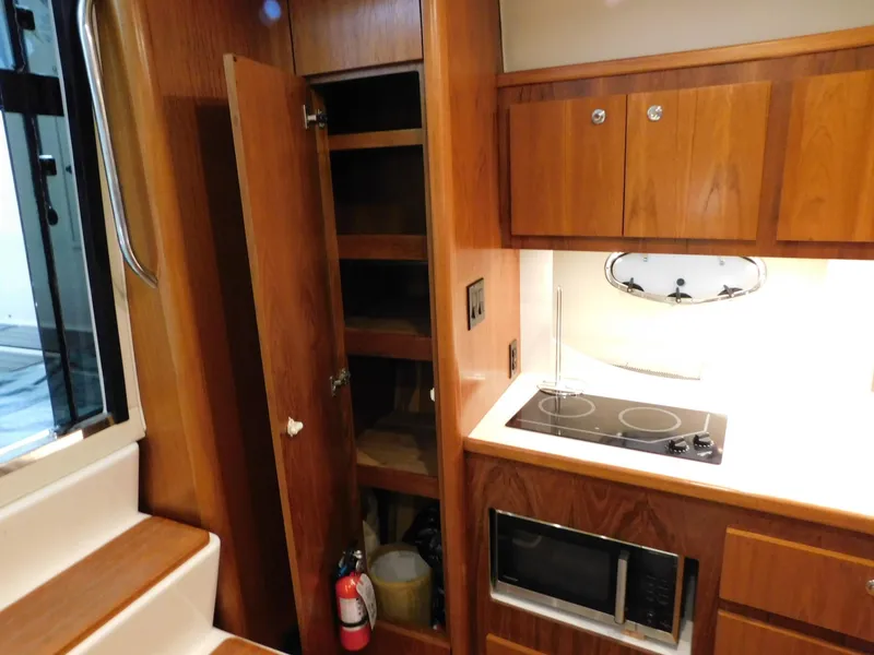 Slide: The Image of 1999 Tiara Yachts 3500 Express interior kitchen with stove, microwave, and wooden cabinets. - 31
