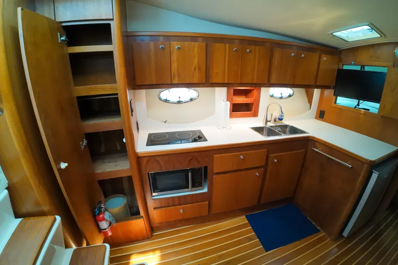 Slide: The Image of 1999 Tiara Yachts 3500 Express galley with wooden cabinets, stove, sink, and microwave. - 99