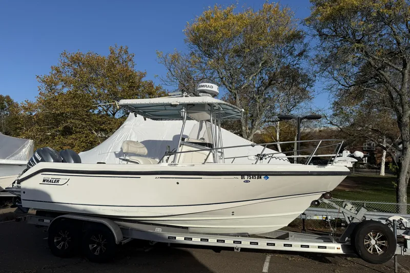 Slide: The Image of 2001 Boston Whaler 230 Outrage boat on trailer, parked outdoors with trees in background. - 0