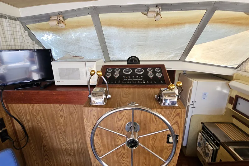 Slide: The Image of 1980 Bertram 42 Convertible helm with steering wheel, control panel, TV, and microwave. - 22