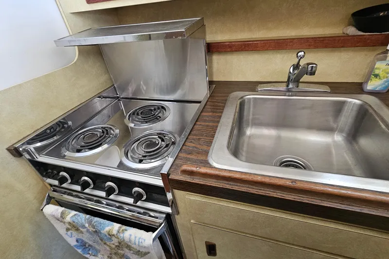 Slide: The Image of 1980 Bertram 42 Convertible kitchen with stove and sink, showcasing compact marine design. - 24