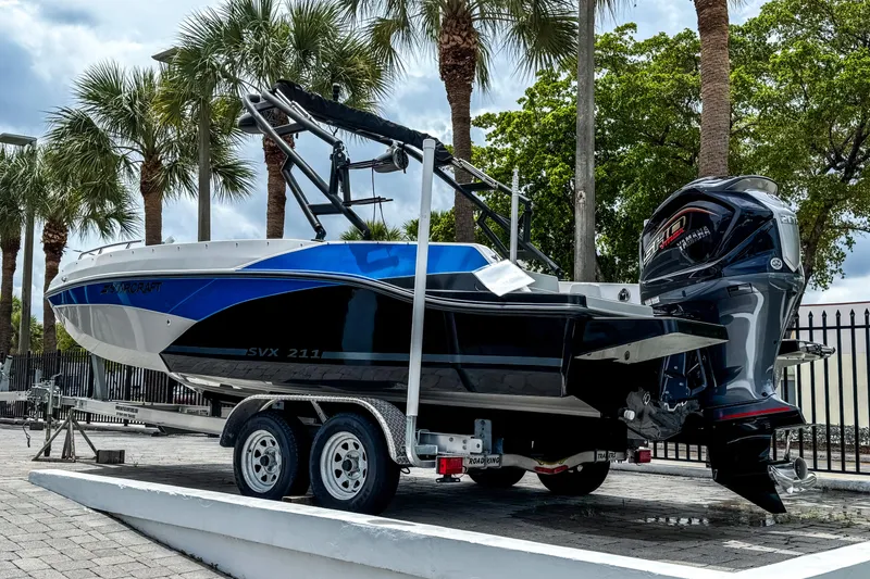 Slide: The Image of 2024 Starcraft SVX 211 OB boat on trailer, parked outdoors with palm trees. - 4