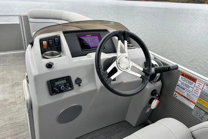 Slide: The Image of 2023 Bennington 22 SSR boat dashboard with steering wheel and control panel on a lake. - 10