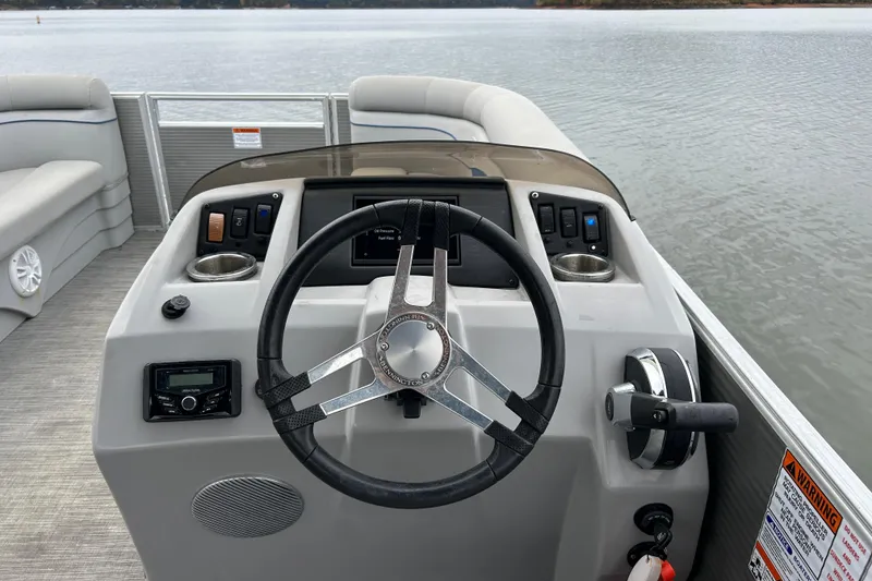 Slide: The Image of 2023 Bennington 22 SSR boat dashboard with steering wheel and controls on a calm lake. - 11