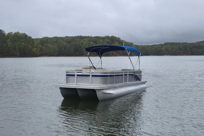 Slide: The Image of 2023 Bennington 22 SSR pontoon boat on a calm lake with forested shoreline. - 4