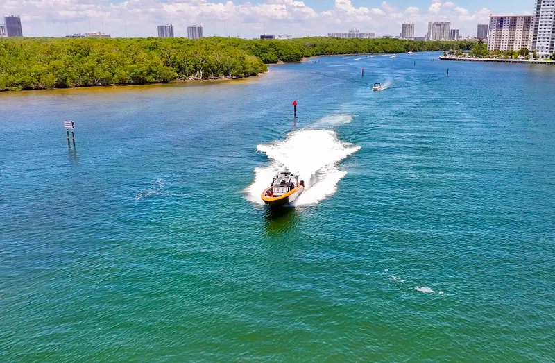 Slide: The Image of 2022 Midnight Express 43 Open cruising on a scenic waterway with lush greenery and cityscape. - 17