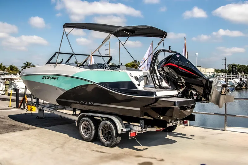 Slide: The Image of 2024 Starcraft SVX 230 OB boat on trailer by marina under blue sky. - 2
