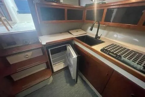 Slide: The Image of 1988 Albin 34 Cruiser kitchen with open fridge, sink, and wooden cabinets. - 35