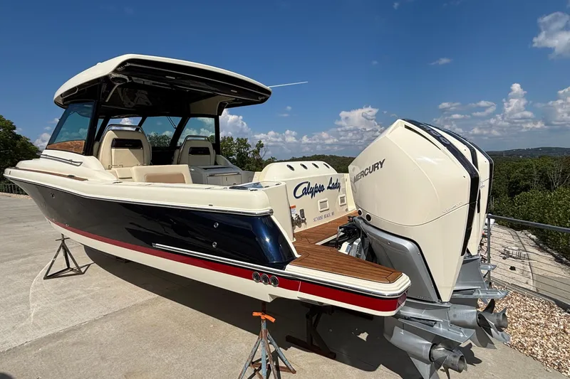 Slide: The Image of 2021 Chris-Craft Calypso 35 boat with dual Mercury engines, docked outdoors under a clear sky. - 64