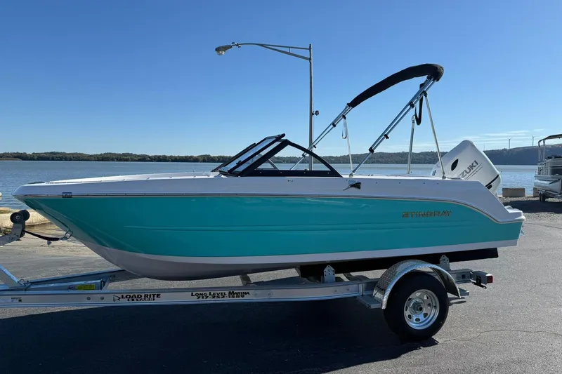 The Image of 2026 Stingray 172 DC boat on trailer by waterfront, clear sky background. - 1