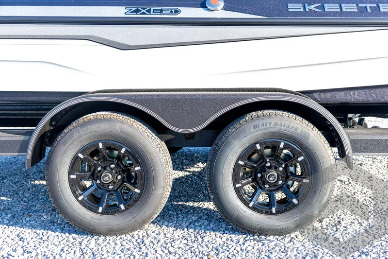 Slide: The Image of 2026 Skeeter ZXE21 trailer with dual black alloy wheels on gravel surface. - 34